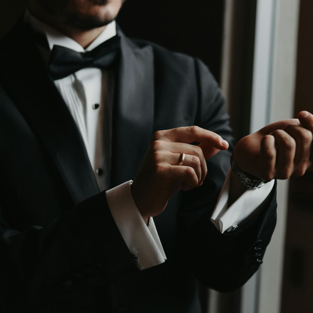 Elegant man in tuxedo, adjusts his wristwatch, showcasing sophisticated men's fashion and formal wear for special occasions.