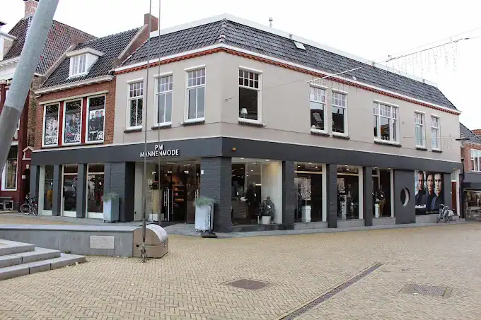 Moderne kledingwinkel voor heren, PM Mannenmode, gelegen in een historisch winkelpand met grote ramen en trendy uitstraling.